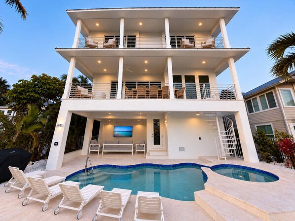 A two-story house with a swimming pool, outdoor seating, and a TV screen. - Drift House · 2026 Luxury 6 King Suites Boat Dock (Fort Myers Beach)