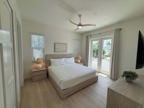 Ein Schlafzimmer mit Bett, Nachttischlampen, Deckenventilator, Fernseher und einem Fenster mit Jalousien.