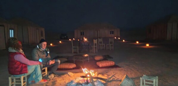A group of people seated around a campfire in an open area with tents in the background. - starlitdesertcamp (Foum Zguid)