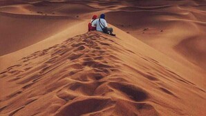 A desert landscape with sand dunes and a person sitting on a dune. - starlitdesertcamp (Foum Zguid)