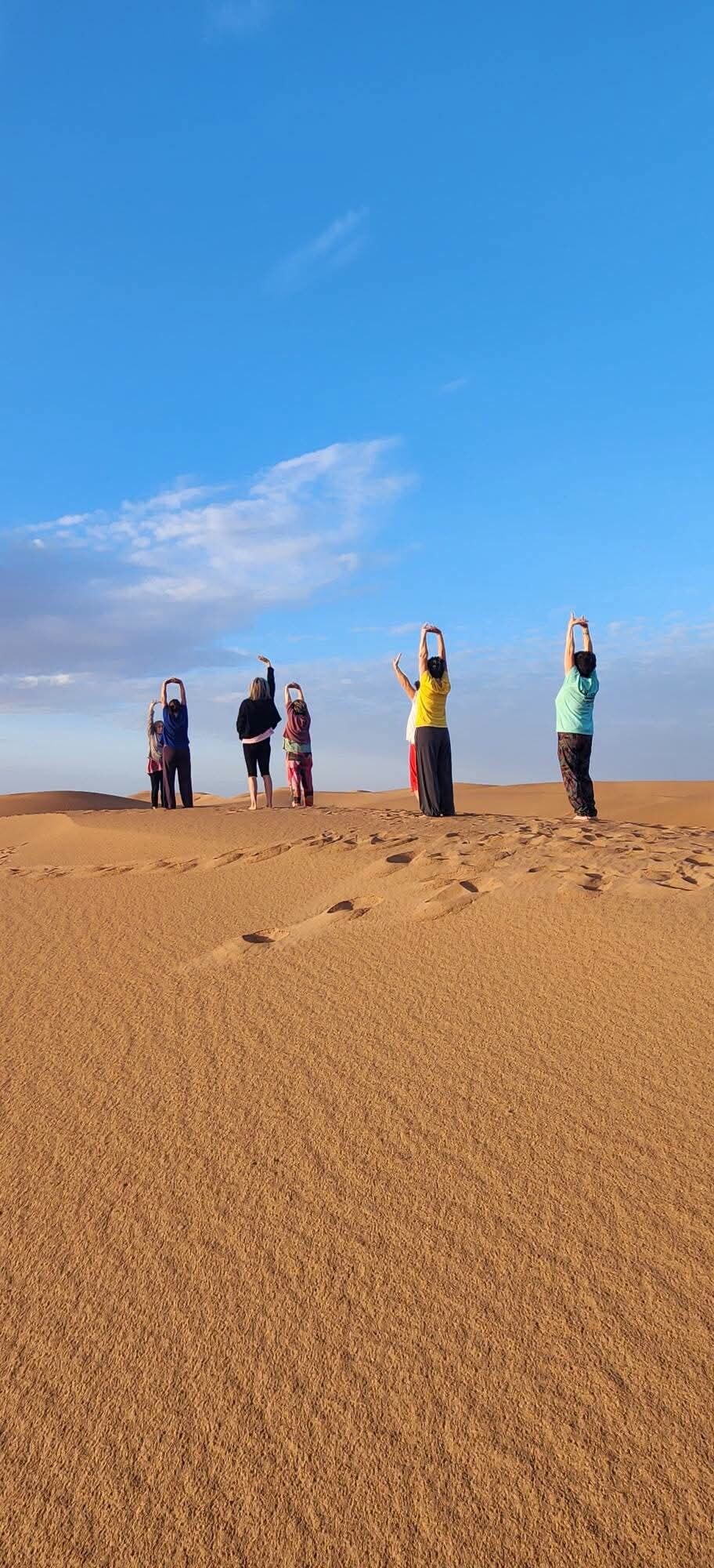 Eine Gruppe von Menschen dehnt sich auf einem sandigen Strand unter blauem Himmel aus.