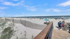 Una spiaggia con una passerella in legno che conduce alla riva, dune sabbiose e ombrelloni.