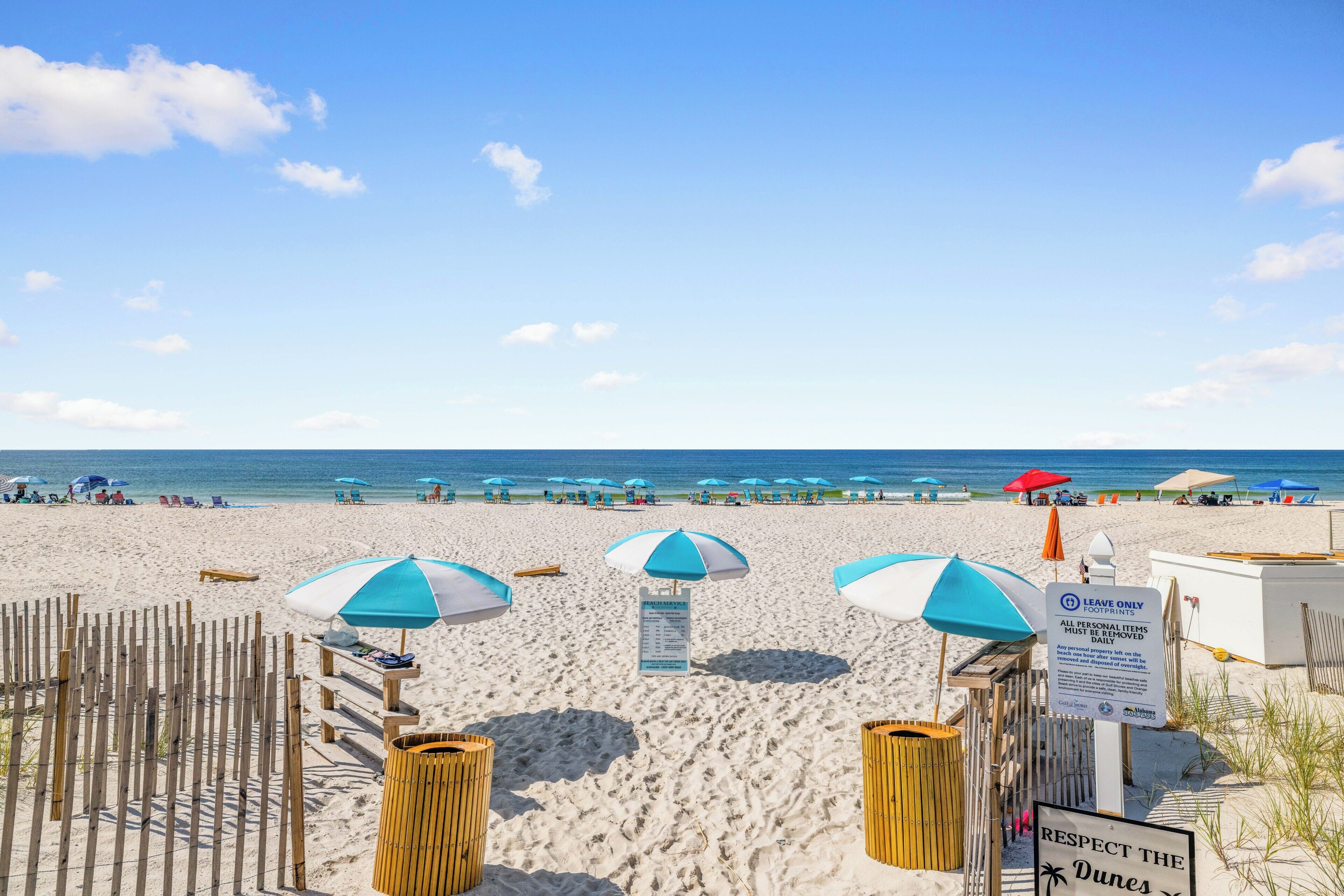 Une plage avec des parasols, un panneau indiquant la présence d’un service de plage, et un autre panneau rappelant qu’il ne faut laisser que ses empreintes.