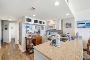 A modern kitchen with white cabinets, a granite countertop, and a microwave. - Gulf Shores Surf and Racquet 204A- Fisherman's Paradise by Liquid Life (Gulf Shores)
