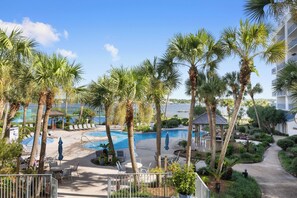 A resort pool area with palm trees, lounge chairs, and a view of the water. - Gulf Shores Surf and Racquet 204A- Fisherman's Paradise by Liquid Life (Gulf Shores)