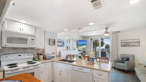 Una cucina moderna con mobili bianchi, forno a microonde, piano cottura e lavastoviglie. C'è una zona pranzo con tavolo e sedie in legno.
