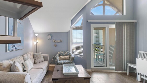 Een woonkamer met een bank, een gestreept fauteuil, een salontafel en een balkon met uitzicht.