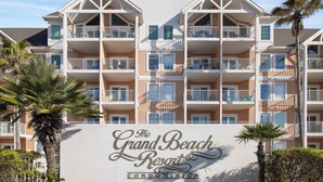Een meerhoog gebouw met balkons, palmbomen en een bord met de tekst 'The Grand Beach Resort Condominium'.