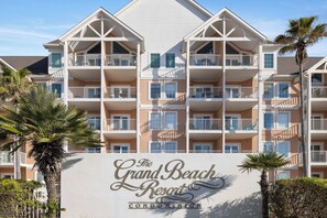 Ein mehrstöckiges Gebäude mit Balkonen, Palmen und einem Schild mit der Aufschrift 'The Grand Beach Resort Condominium'.