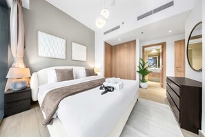 A modern hotel room with a large bed, bedside tables, a mirror, a dresser, and a potted plant. - Free Housekeeping Visits During Your Stay - Stayshort - Contemporary 2 Bed Retreat in Meydan for 6 (Dubai)