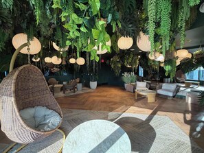 Een kamer met hangplanten, rieten meubels en hanglampen.
