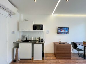 A compact kitchenette with a microwave, sink, and small refrigerator. A TV is mounted on the wall, and there is a wooden cabinet and a chair. - UrbanFlat 208 - 249 Saint Denis (París)