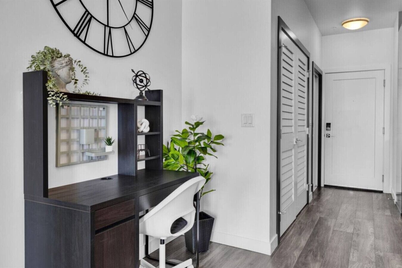 Un intérieur moderne avec un bureau en bois foncé, une chaise blanche, une grande horloge et une plante.