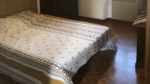 Ein Schlafzimmer mit einem Bett, einer Kommode, einem Fenster mit Vorhängen, einer Wandlampe und einem Poster.