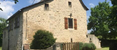 A stone building with a pitched roof, a small window with shutters, and a wooden gate.