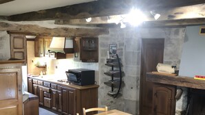 Eine rustikale Küche mit Holzschnitzschränken, einer Mittelinsel, einem Esstisch mit Stühlen und einer Wand aus Stein.