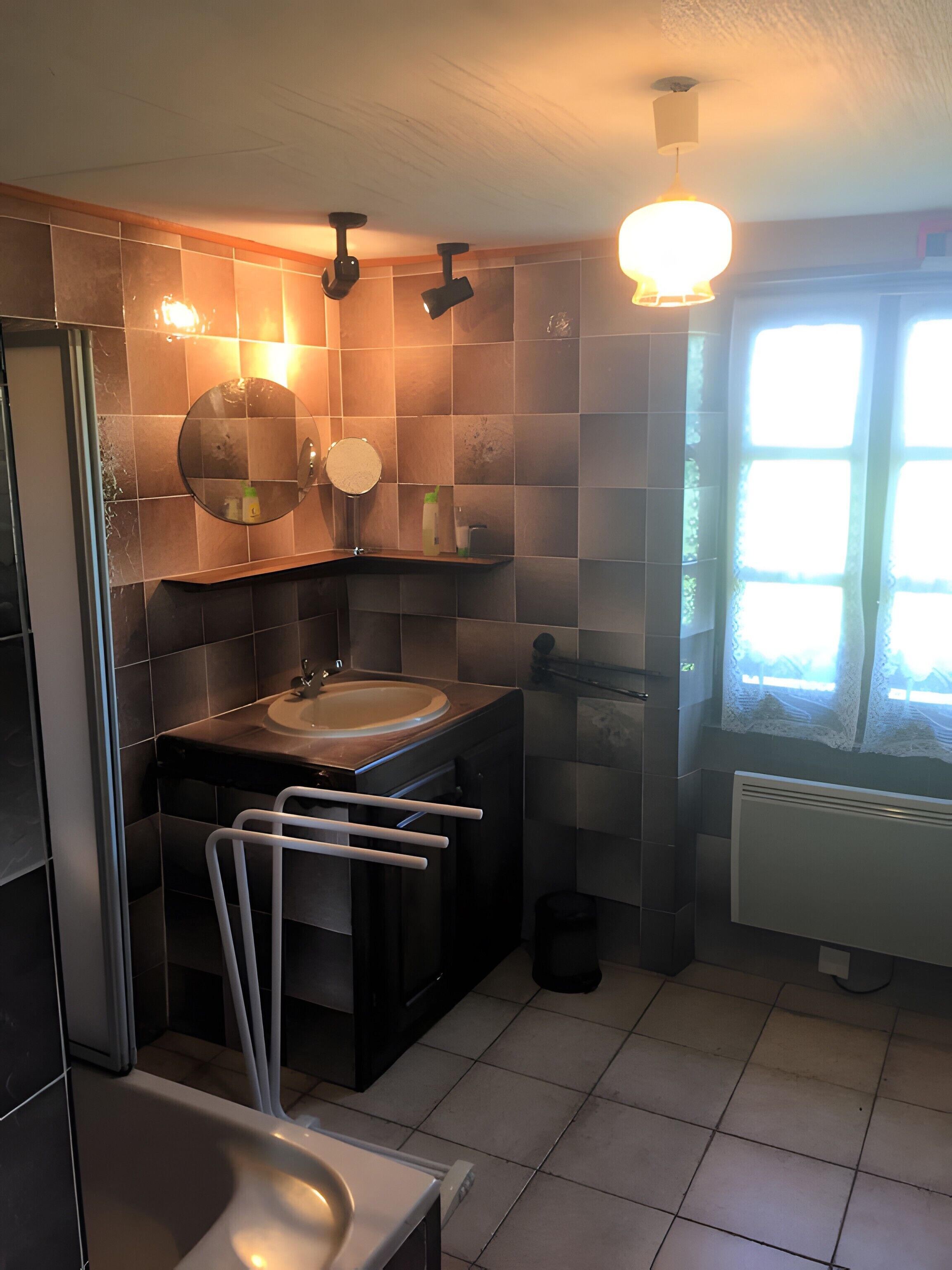 Een badkamer met een wastafel, spiegel, handdoekhouder en een raam met kantgordijnen.