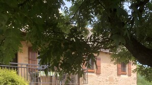 Ein Steinhaus mit Balkon, einem Glastisch mit Stühlen und einem Rasen.