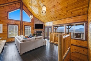 A spacious living room with a fireplace, wooden floors, and large windows offering mountain views. - 4BR, Views, Hot Tub, Gatlinburg, Evergreen Cabin (Gatlinburg)
