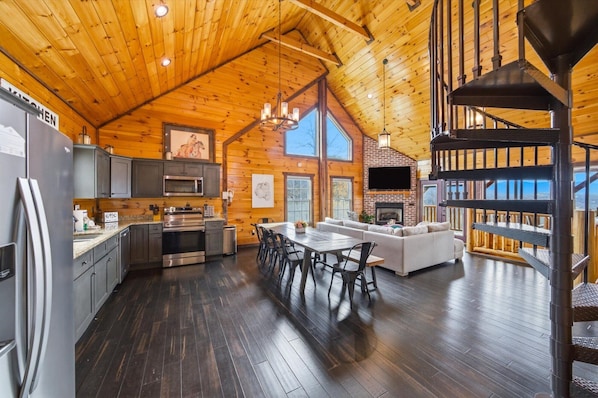 A spacious log cabin interior with a kitchen, dining area, and living room, featuring wooden floors and a fireplace. - 4BR, Views, Hot Tub, Gatlinburg, Evergreen Cabin (Gatlinburg)