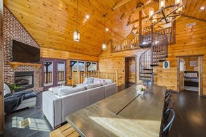 A log cabin interior with a fireplace, a sofa, a dining table, and a spiral staircase. - 4BR, Views, Hot Tub, Gatlinburg, Evergreen Cabin (Gatlinburg)