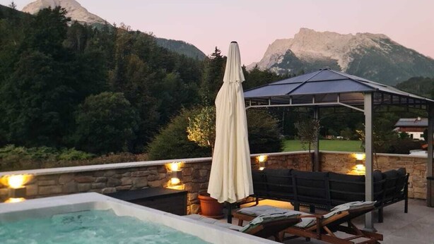 Un bain à remous avec vue sur les montagnes, un espace détente couvert avec une table et un parasol blanc.