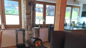 Un salon chaleureux avec une cheminée en pierre, un canapé et une vue sur l’extérieur grâce à de grandes fenêtres.