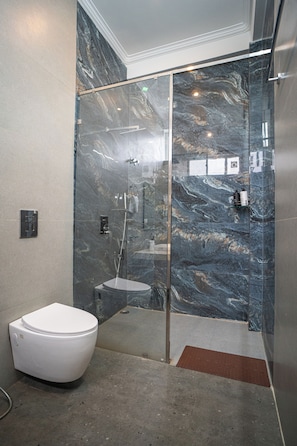 Een moderne badkamer met een douchecabine van glas, een wit toilet en een marmeren wand.