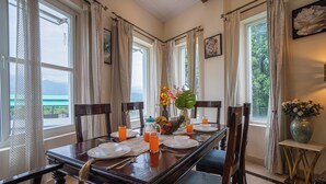 Un coin repas avec une table dressée pour quatre personnes, des chaises, un vase rempli de fleurs et une vue sur la mer.