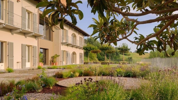 Ein Gebäude mit mehreren Balkonen, ein Garten mit unterschiedlichen Pflanzen und ein klarer Himmel.