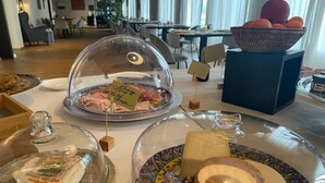 Ein Buffet mit verschiedenen Käsesorten und Fleischwaren unter Glasglocken, eine Obstkorb und eine dekorative Schale auf einem Tisch in einem Hotelrestaurant.