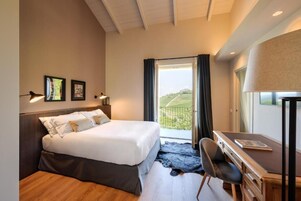 Quarto com cama, escrivaninha, cadeira e vista para o exterior.