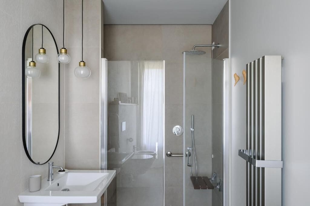 Une salle de bain moderne avec une douche à parois de verre, un lavabo blanc et un miroir agrémenté de luminaires suspendus.