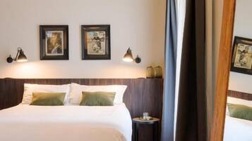 A hotel room with a bed, a small table, a mirror, and framed pictures on the wall.
