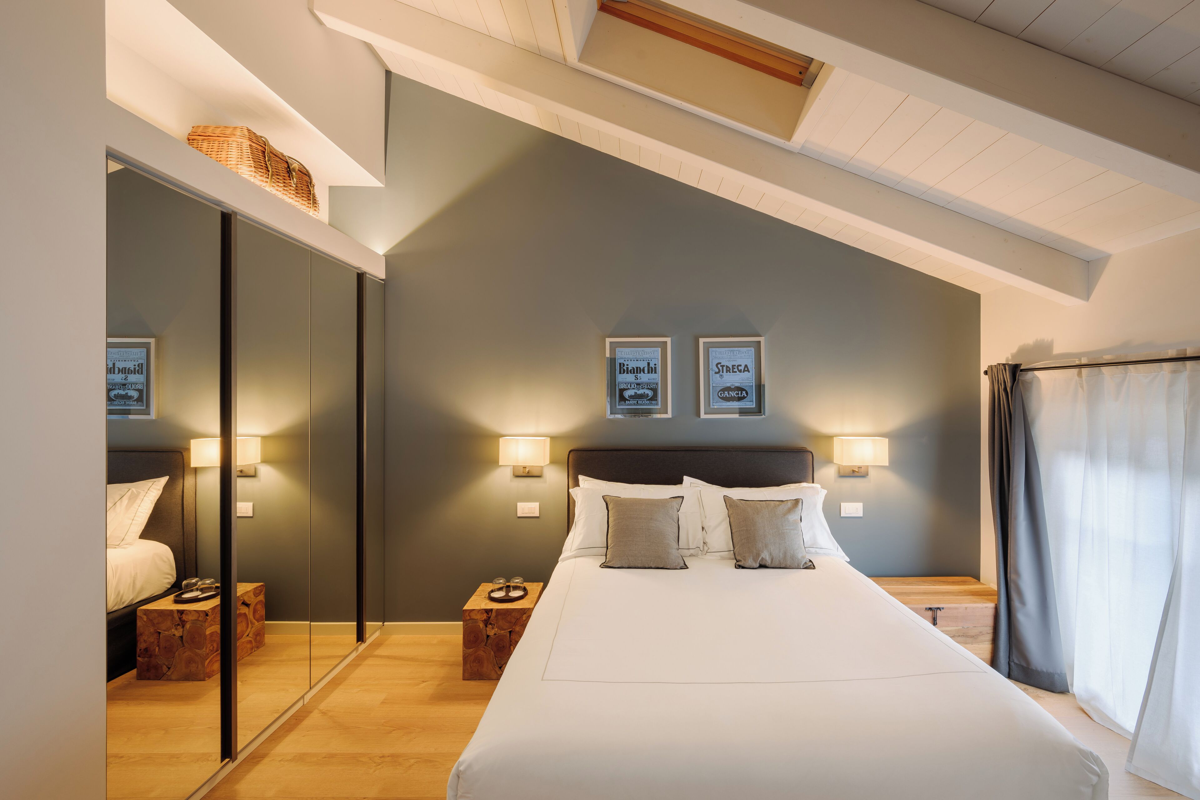 Een moderne hotelkamer met een groot bed, nachtkastjes, een spiegel en ingelijste foto’s aan de muur.