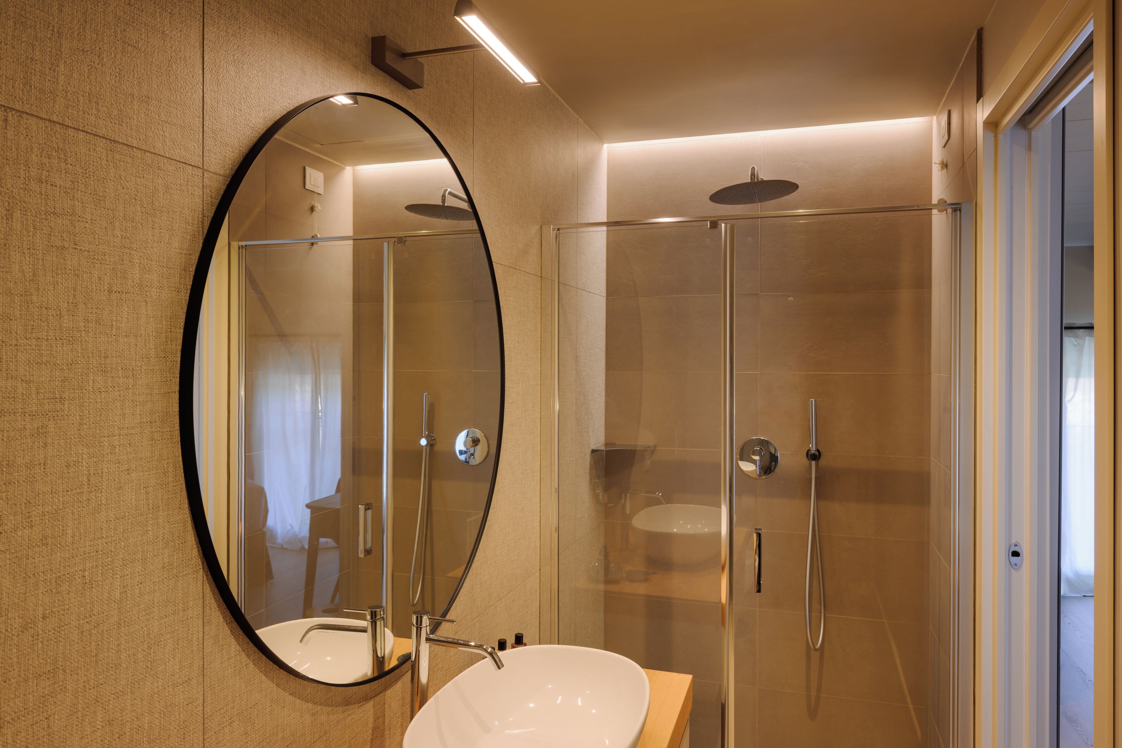 Een moderne badkamer met een ronde spiegel, een wastafel en een douche met glazen wanden.