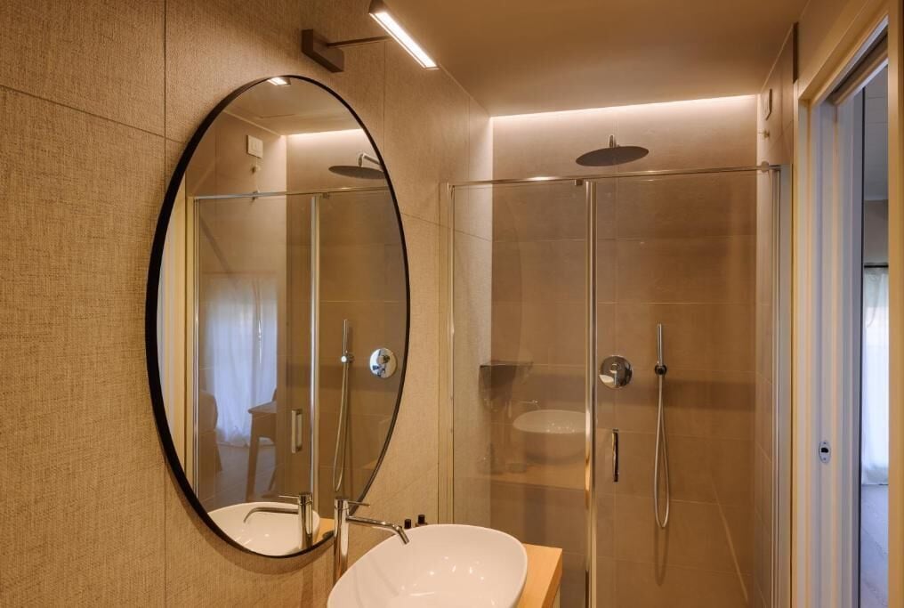Casa de banho moderna com um espelho redondo, uma sanita branca e cabine de duche em vidro.