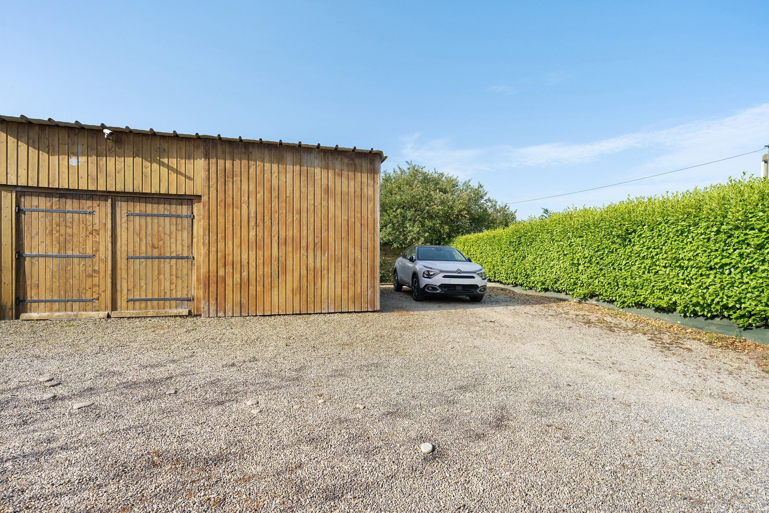 A gravel driveway leading to a wooden building with two large doors.