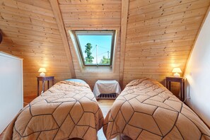 Ein Zimmer mit Holzwänden und geneigter Decke, mit zwei Betten mit passenden Bettdecken, einem Oberlicht und zwei Nachttischlampen.