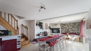 Un espace repas comprenant une table, des chaises, un escalier, une cuisine et un mur en pierre.