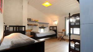 Une chambre avec trois lits, un bureau, des étagères remplies de livres et une fenêtre.