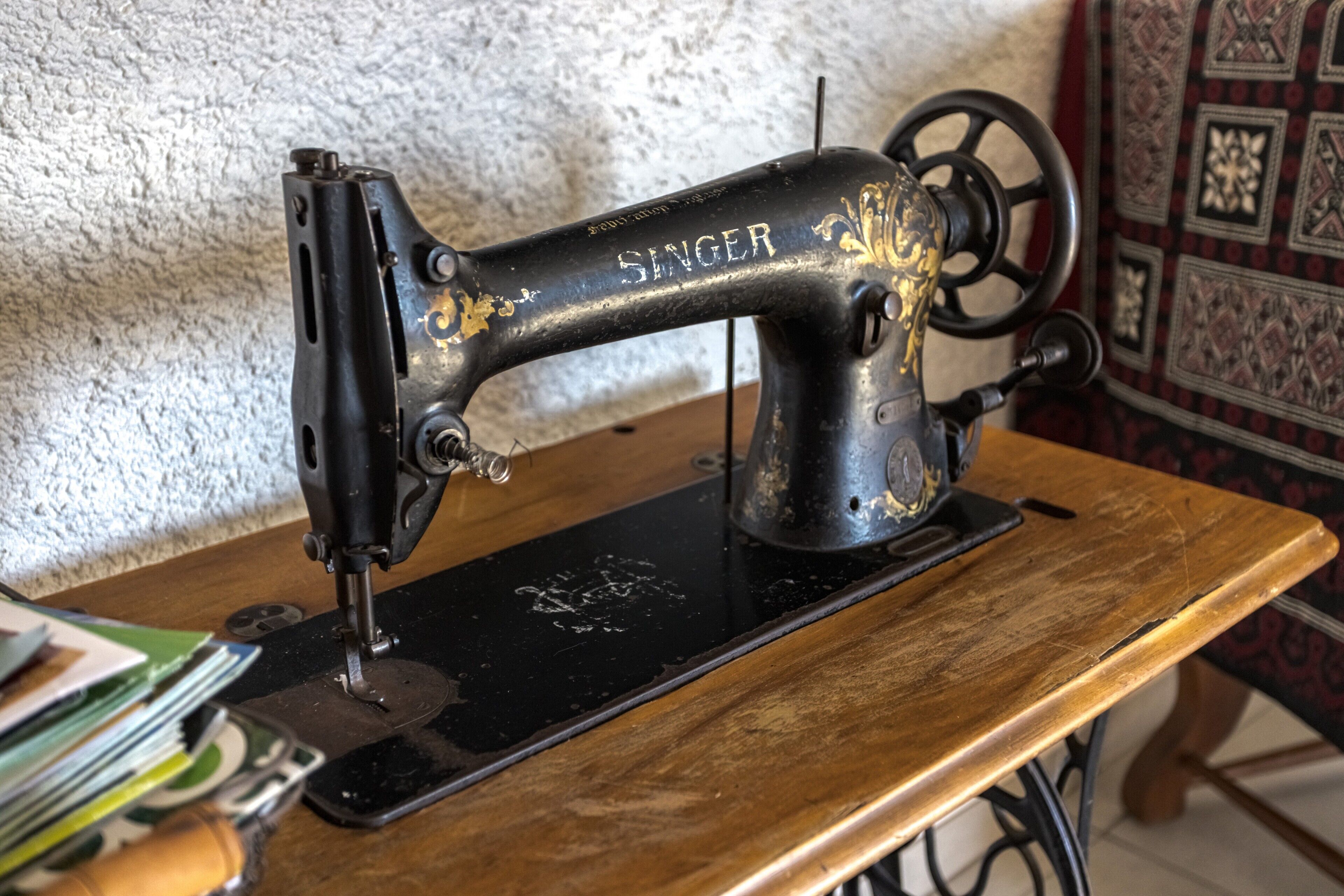 Una macchina da cucire Singer su un tavolo di legno, con una parete strutturata sullo sfondo.