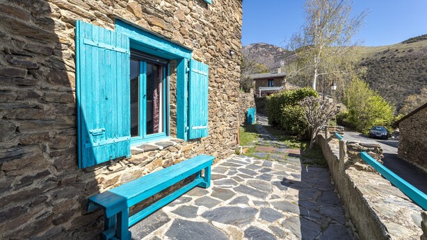 Un bâtiment en pierre doté d’une terrasse pavée, d’un banc en bois et offrant une vue sur une colline.