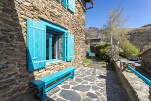 A stone building with a stone-paved patio, a wooden bench, and a view of a hillside.