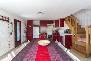 Une cuisine avec des meubles de rangement rouges, un escalier en bois et un coin repas comprenant une table et des chaises.