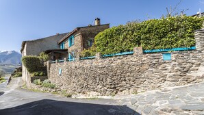 Un bâtiment en pierre avec un mur de pierre, une route et une montagne en arrière-plan.