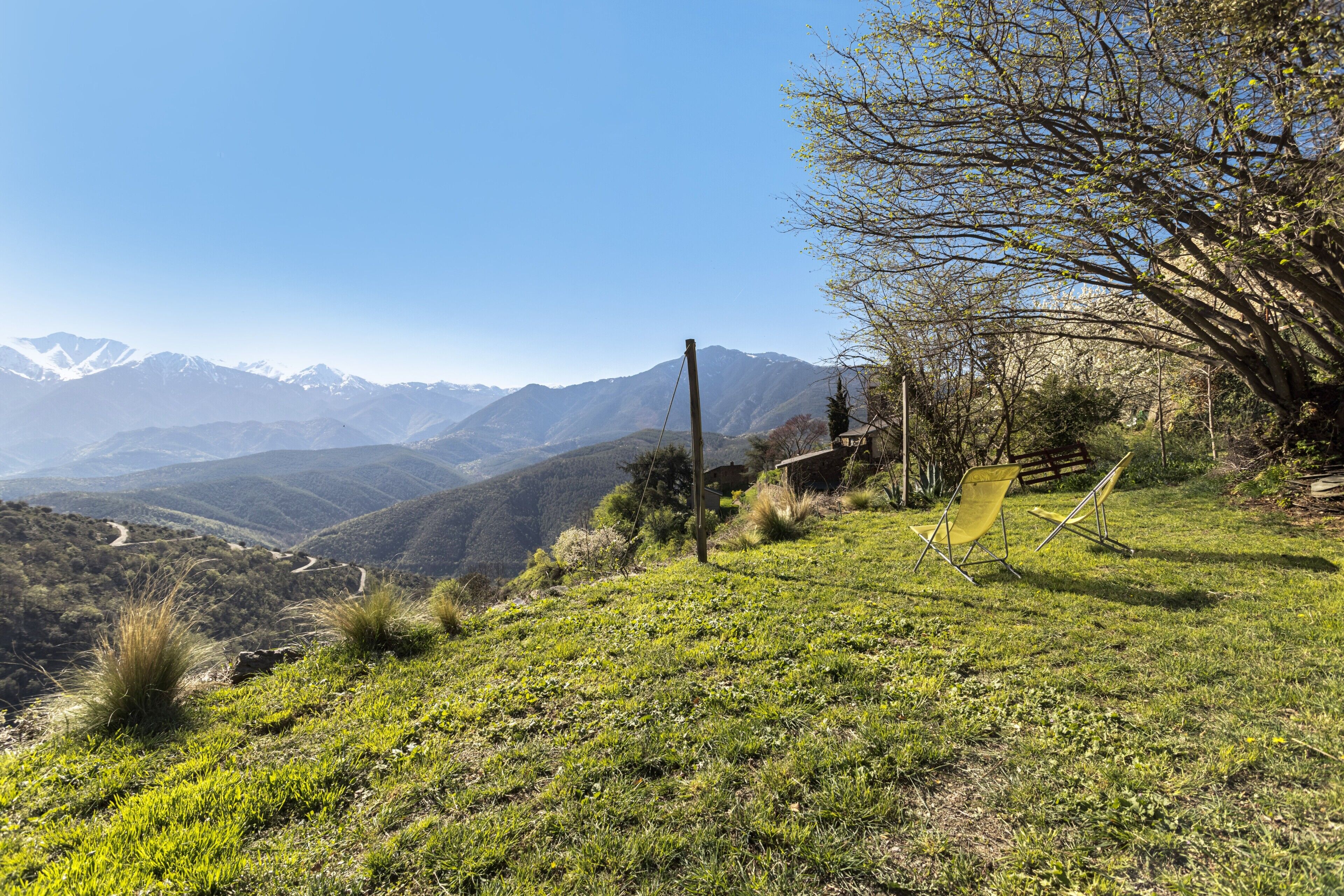 A grassy hillside with a clear view of distant mountains, a wooden fence, and two yellow chairs.