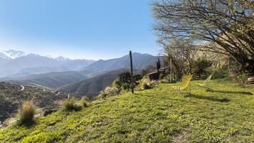 A grassy hillside with a clear view of distant mountains, a wooden fence, and two yellow chairs.