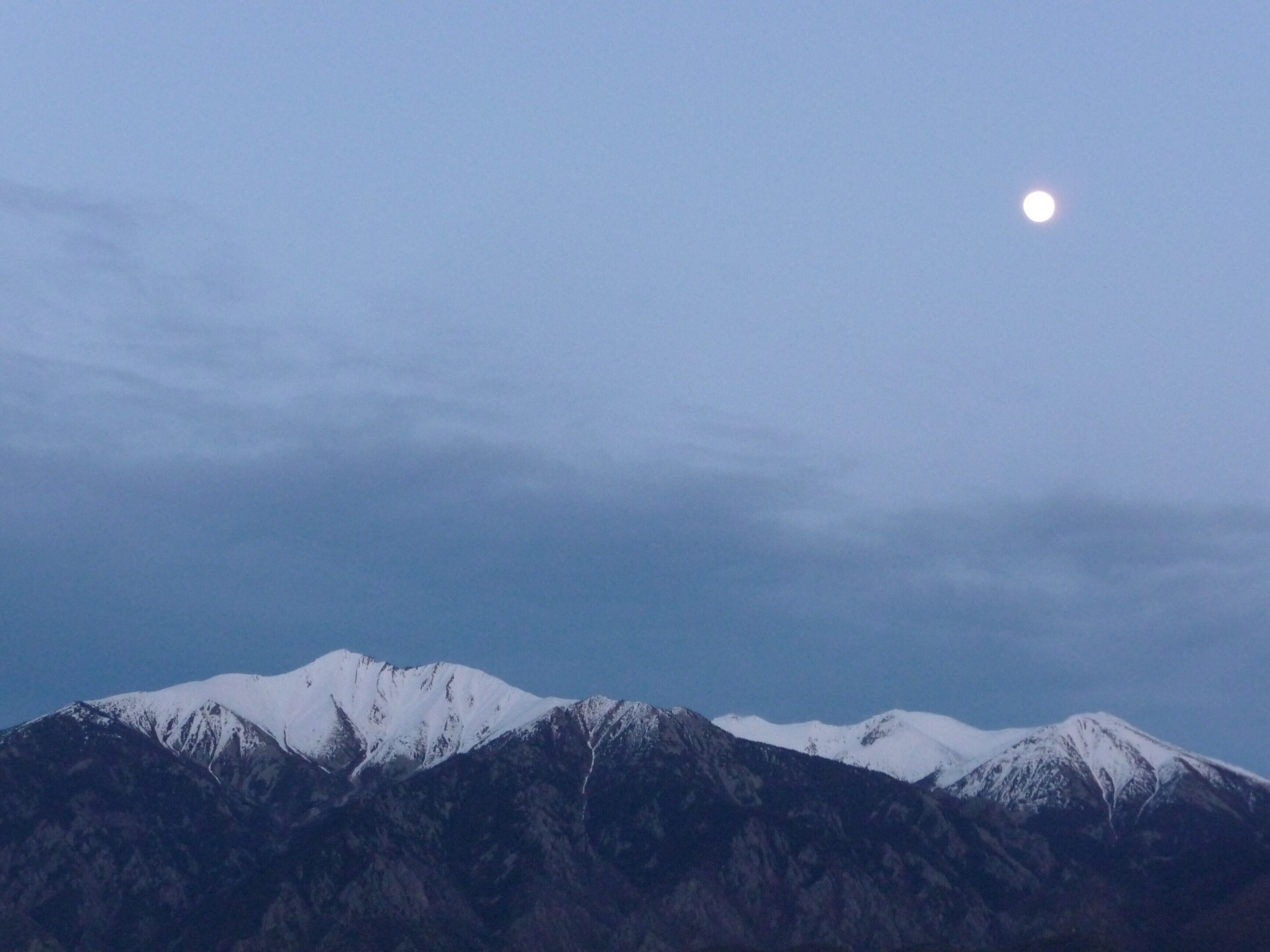 A mountain range with a visible moon in the sky.