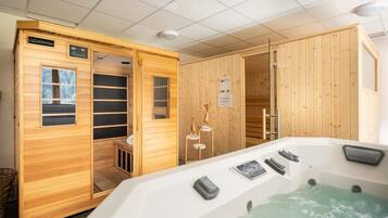A sauna room with a wooden interior, a hot tub with controls, and a wooden door.